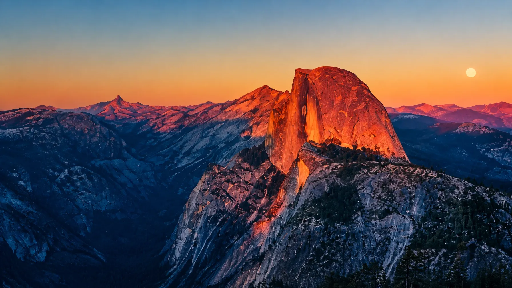 Sunset light on a dramatic granite mountain above a blue valley